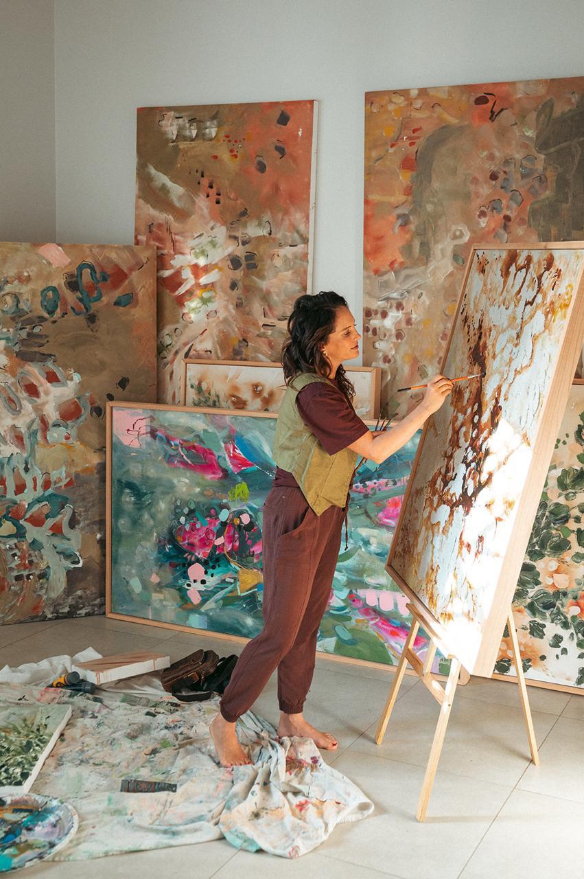 Hayley Lombard painting at her easel in the studio, surrounded by large textured abstract works