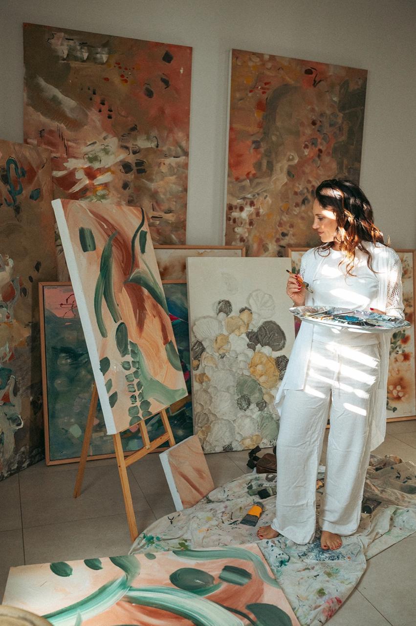 Hayley Lombard at her easel with palette in hand, surrounded by works in progress