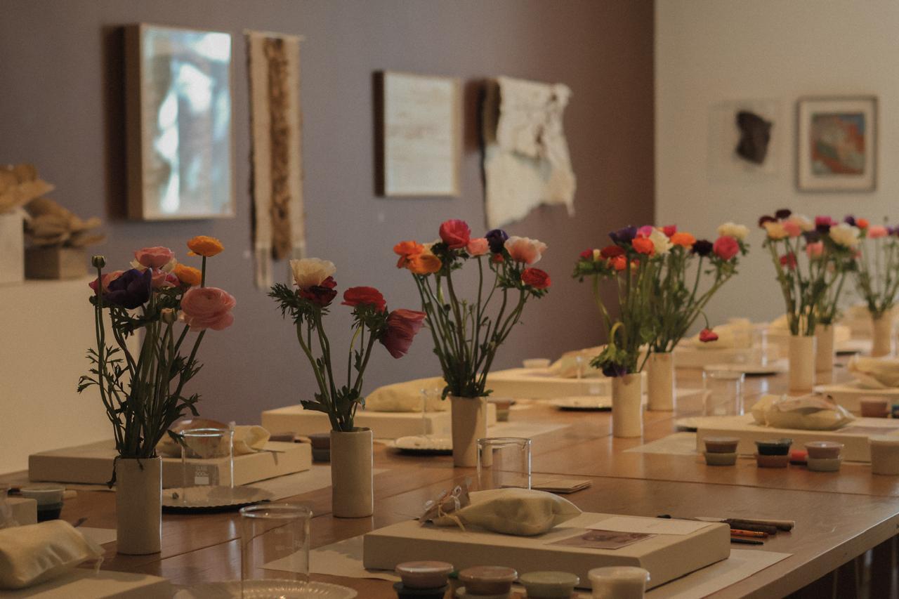 A workshop table set with fresh flowers, paints, and canvases